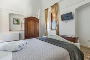 A hotel room with a bed, a wooden wardrobe, a TV mounted on the wall, and a window with curtains.