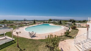 A swimming pool with a curved edge, surrounded by a patio area with outdoor furniture and a view of the countryside. - 3787 ADT - Camera Matrimoniale Luxury (Mottola)