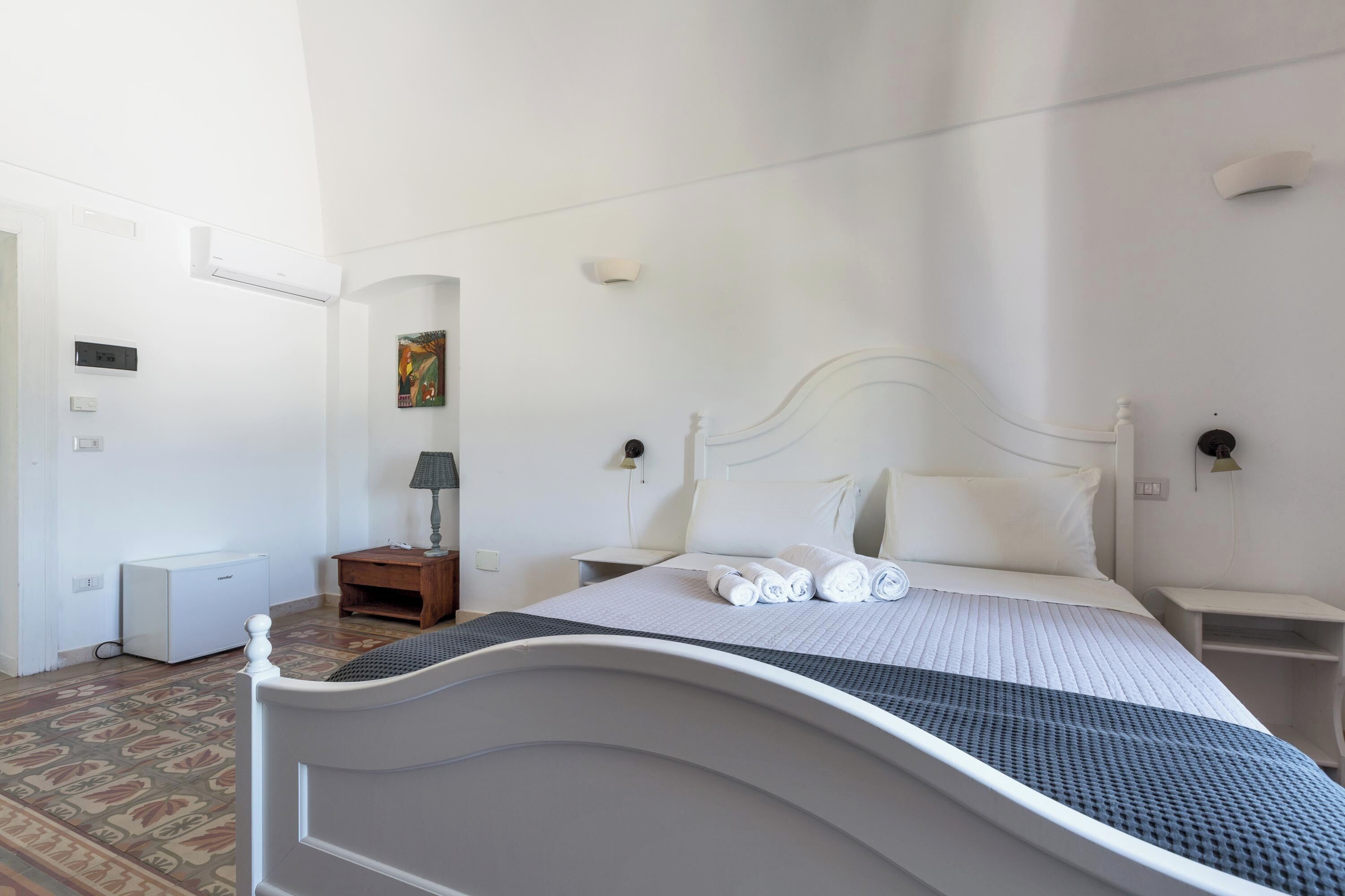Een netjes opgemaakt slaapkamer met een bed, nachtkastjes, een lamp en een radiator.