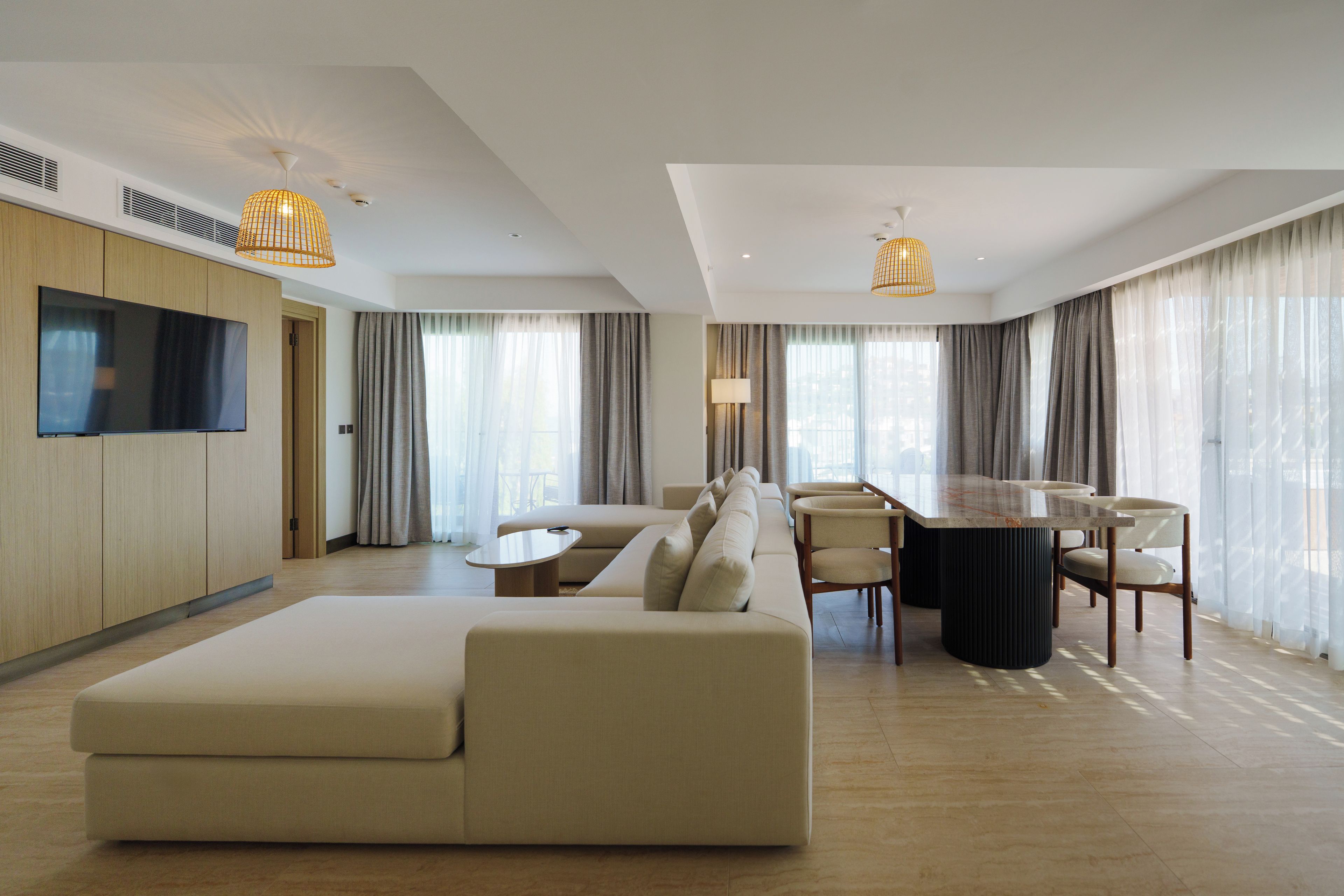 Een moderne hotelkamer met een bank, een eettafel, stoelen en een aan de muur bevestigde televisie.
