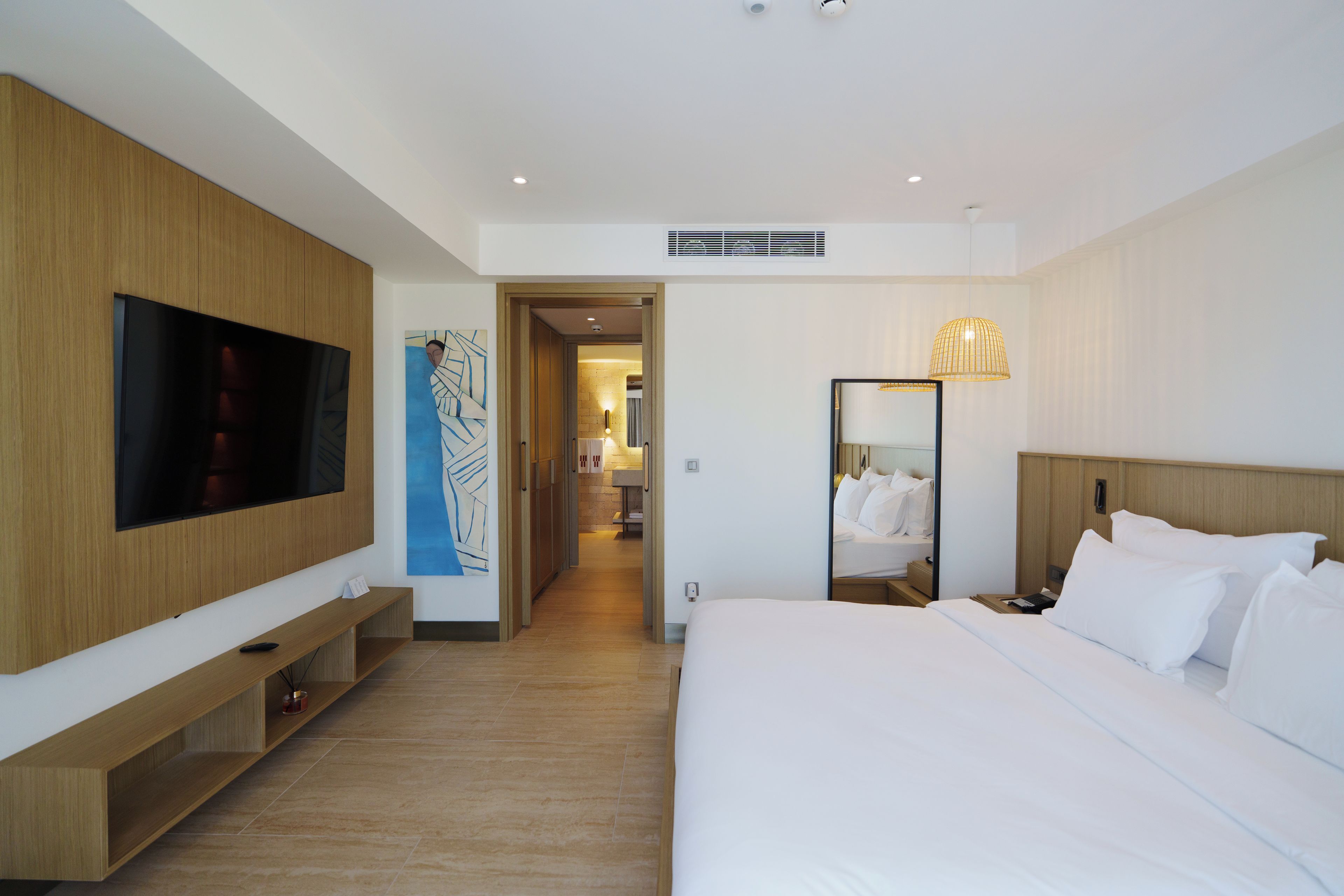 A hotel room with a large bed, a flat-screen TV mounted on the wall, a bedside table, and a mirror.