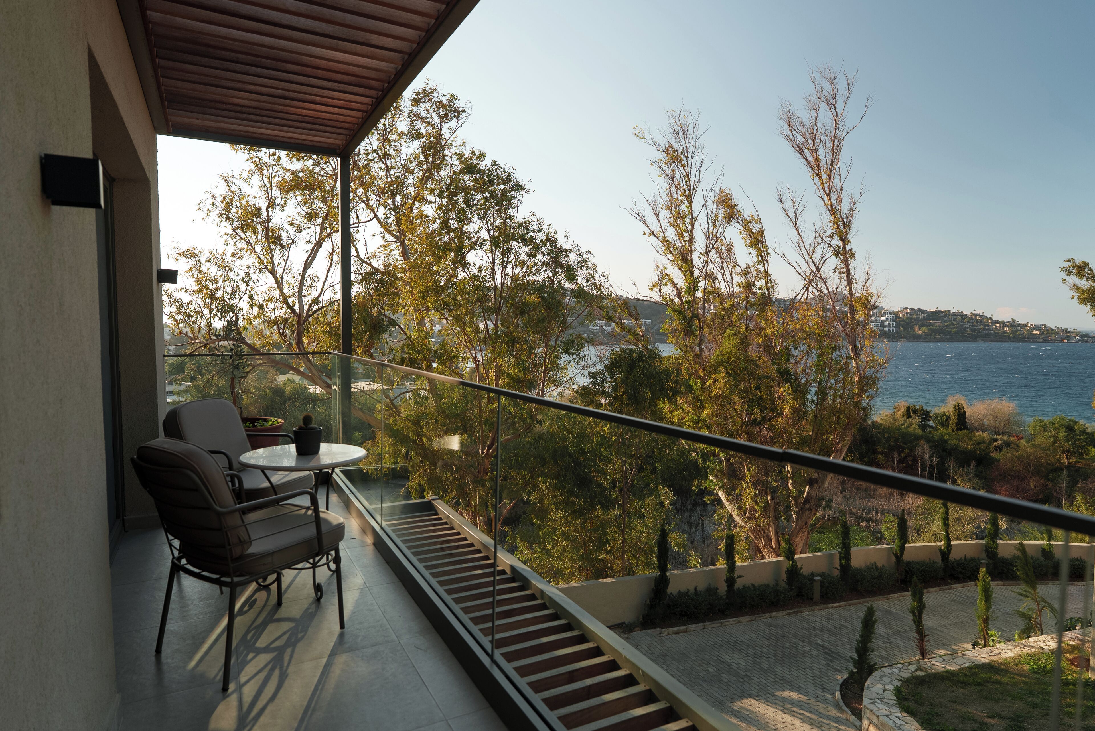 Un balcón con mesa y sillas, con vistas a un paisaje costero con árboles y el mar.