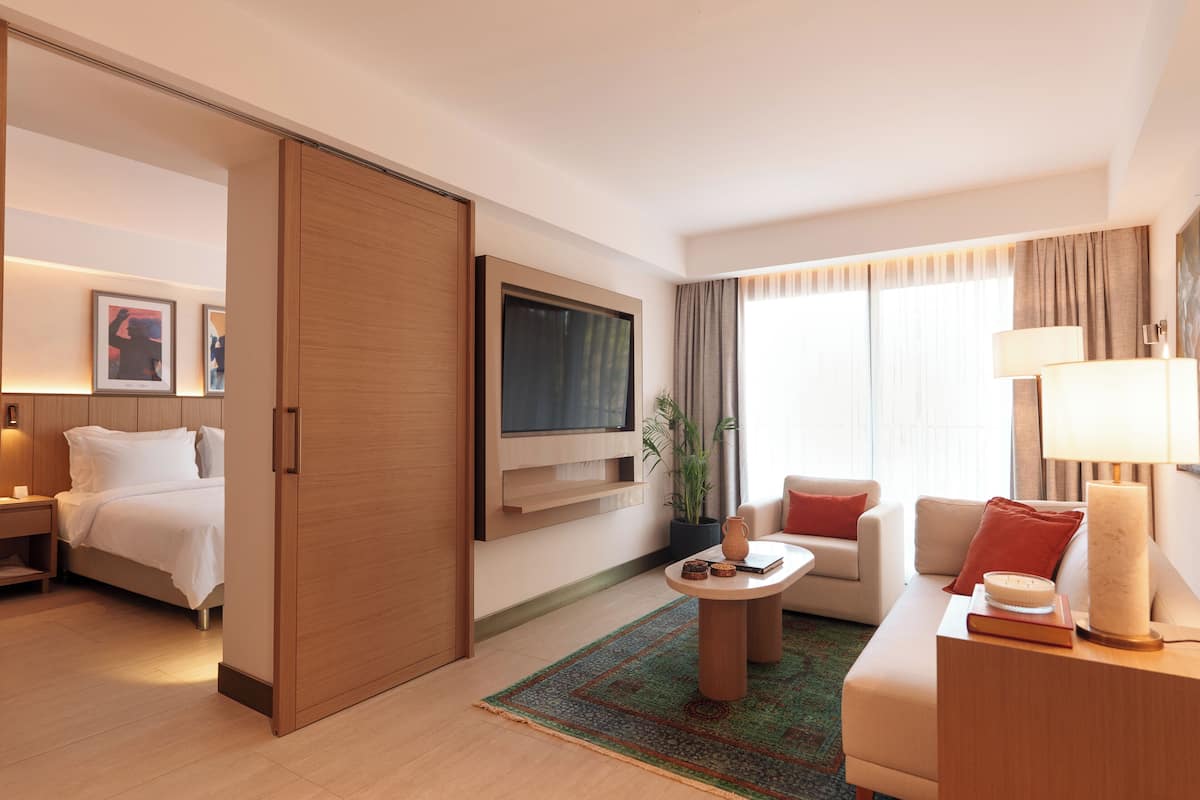 A modern hotel room with a bed, a TV mounted on the wall, a sofa, a coffee table, and a lamp.