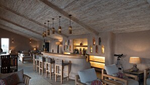 Un vaste espace de vie doté d’un haut plafond et de poutres apparentes, comprenant un coin bar avec des tabourets et une bibliothèque.