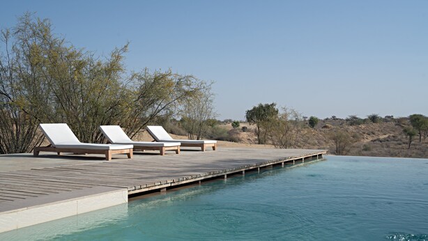 Un espace aménagé au bord de la piscine, avec des chaises longues et une terrasse en bois qui s’étend au-dessus de l’eau.