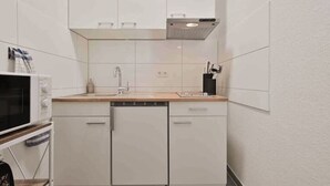 A compact kitchen with white cabinets, a dishwasher, a microwave, and a sink. - Goodliving Apartments Studio Balcony Netflix (Essen)