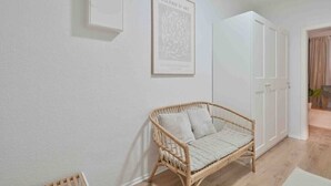 A room with a wicker sofa, a framed artwork on the wall, and a white wardrobe. - Goodliving Apartments Studio Balcony Netflix (Essen)
