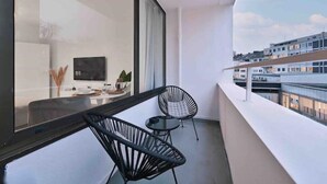 A balcony with two black chairs, a small round table, and a TV on a stand. - Goodliving Apartments Studio Balcony Netflix (Essen)