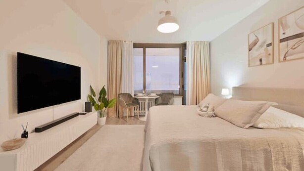 A hotel room with a large bed, a flat-screen TV mounted on the wall, a small table with chairs, and a balcony with curtains. - Goodliving Apartments Studio Balcony Netflix (Essen)