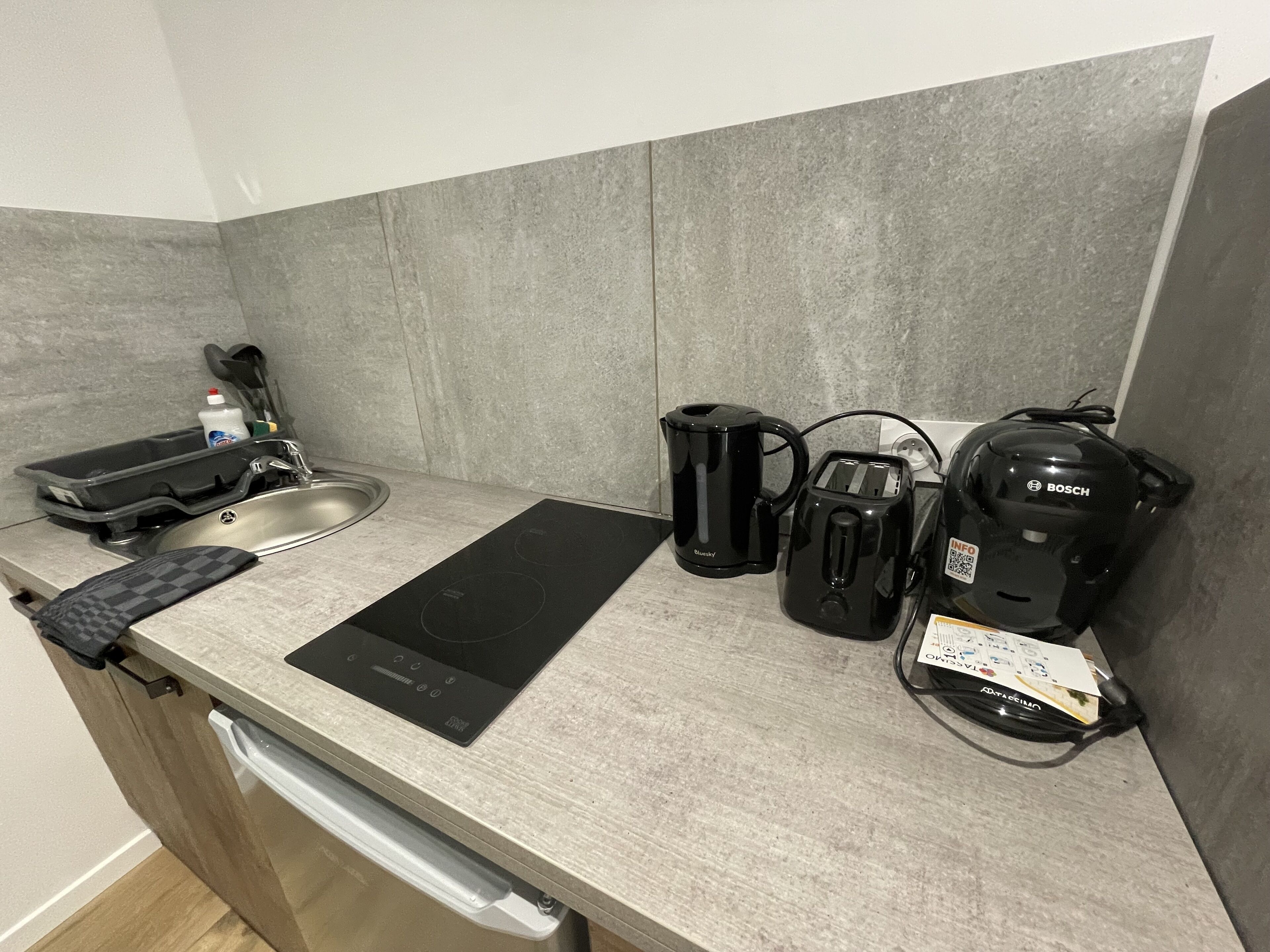 Een keuken met een spoelbak, een zwart inductiekookveld, een Bosch koffiezetapparaat, een broodrooster en een waterkoker.