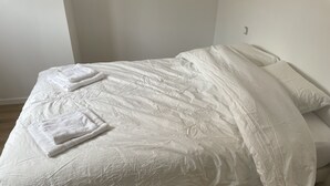 A neatly made bed with white linens and two folded towels on the bed.