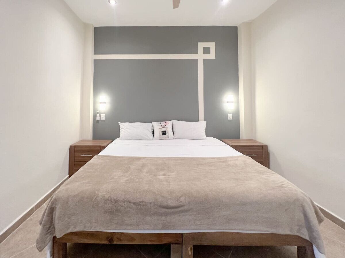 A neatly made bed with a beige blanket in a room with a gray accent wall and two bedside lamps.