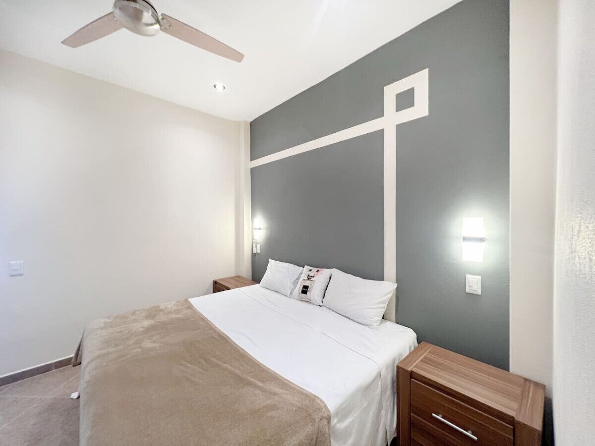 Une chambre à coucher comprenant un lit, des tables de chevet, un ventilateur de plafond et des lampes fixées au mur.