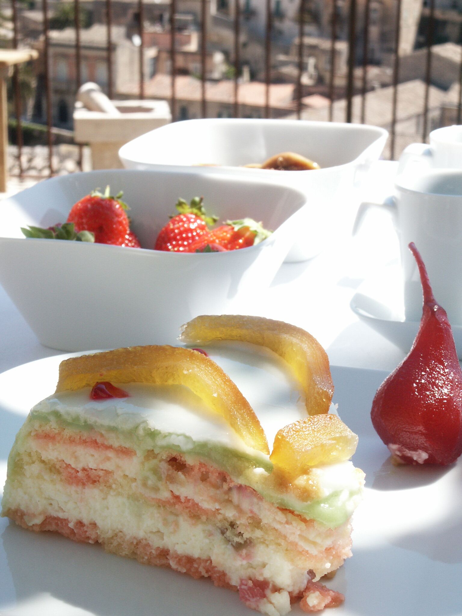 A dessert plate with a slice of layered cake, strawberries, and a red fruit on a white table.