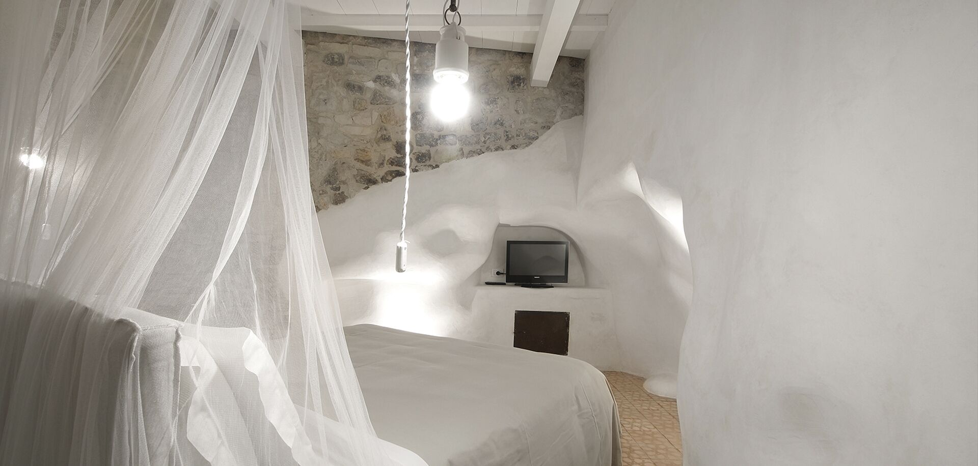 Une chambre à coucher avec un lit, une télévision et un mur en pierre.