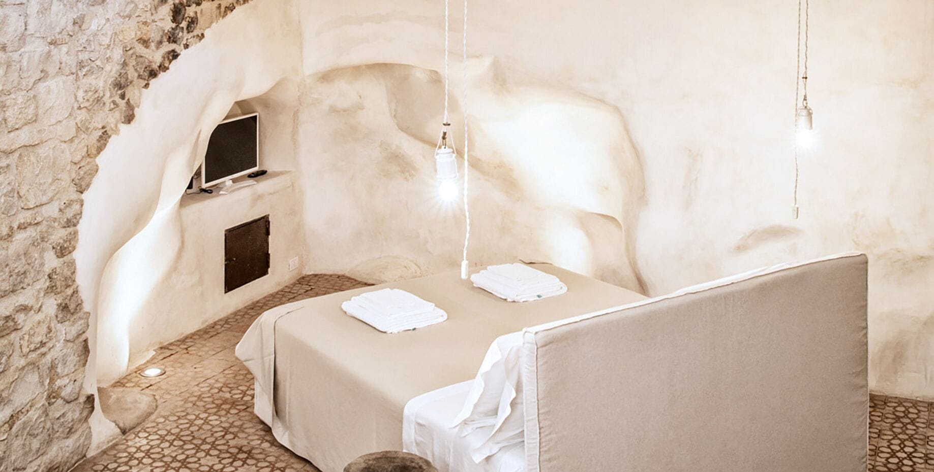 A cozy room with a bed, a small TV, and a stone wall.
