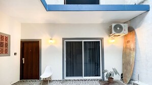 Une pièce avec un sol à motifs, une porte-fenêtre coulissante, une chaise blanche, une planche de surf et une plante en pot.