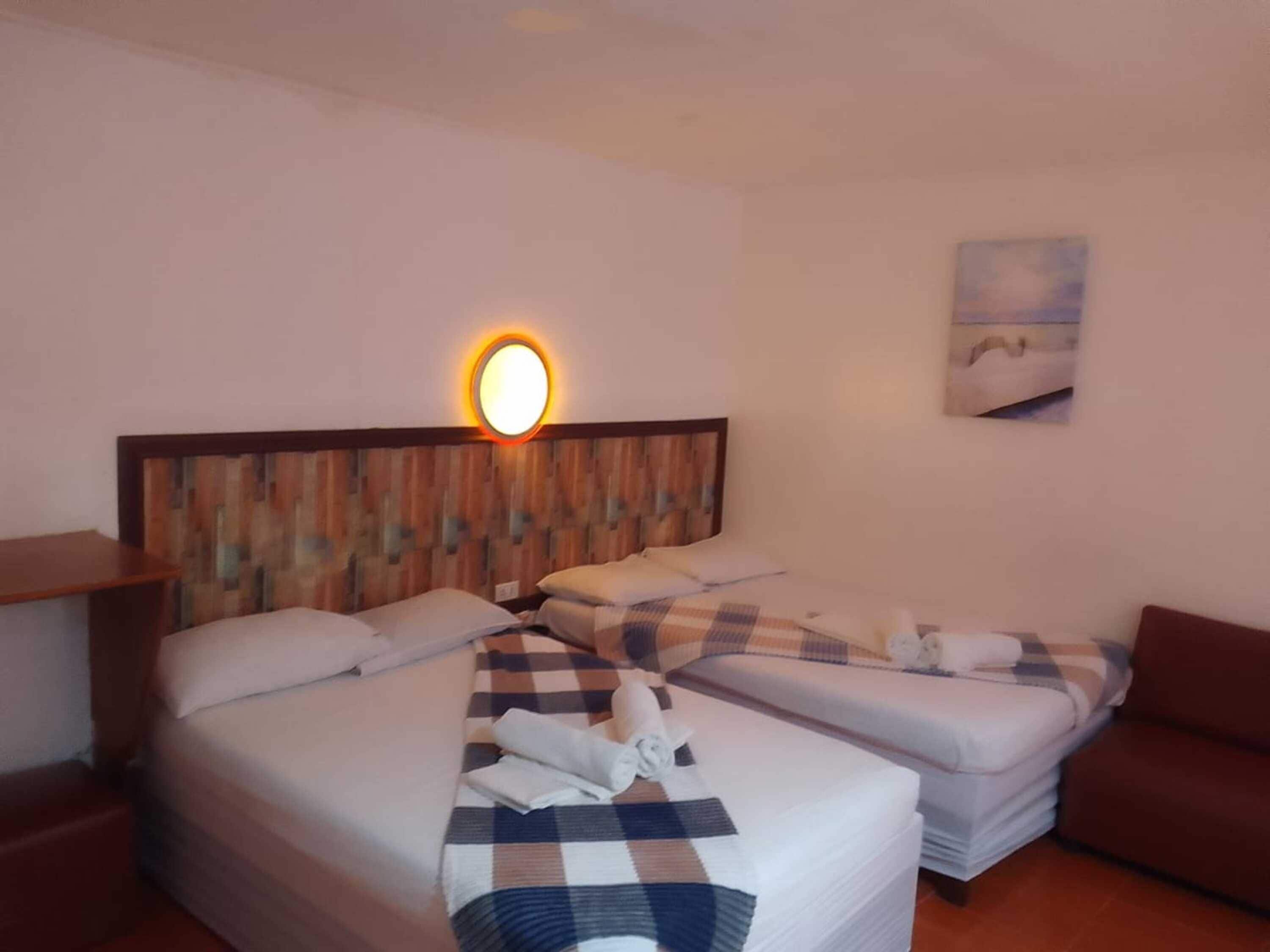 Habitación de hotel con dos camas, cabecero de madera, luz adosada a la pared y un cuadro.