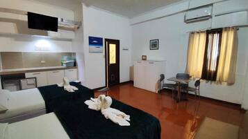 Habitación de hotel con dos camas, un escritorio, una silla, un equipo de aire acondicionado y un televisor.