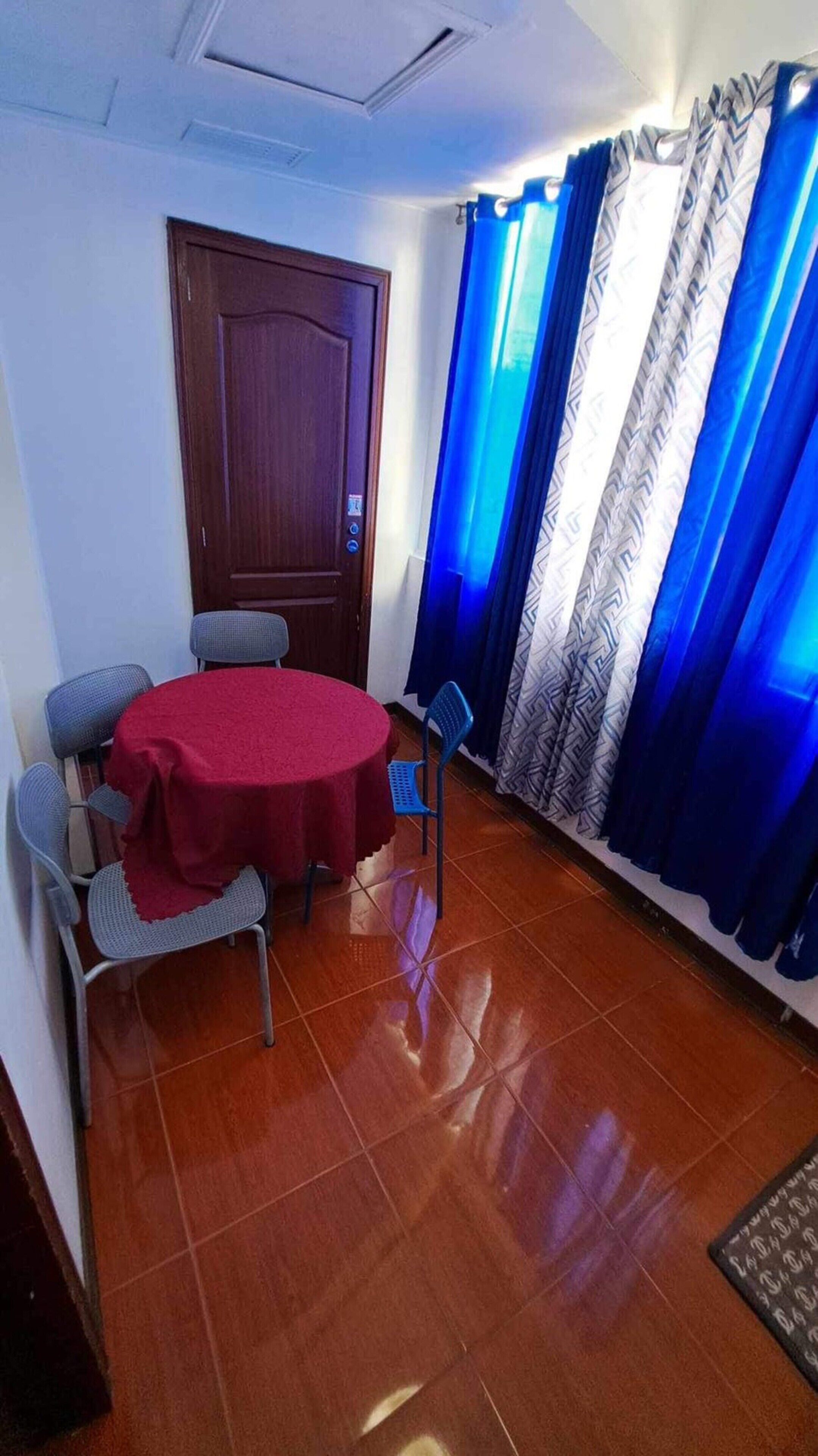 Een kamer met een ronde tafel, vier stoelen, een houten deur en blauwe gordijnen.
