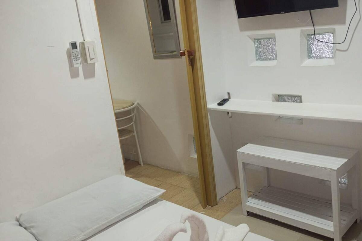 A hotel room with a bed, a TV mounted on the wall, a bedside table, and a small shelf.
