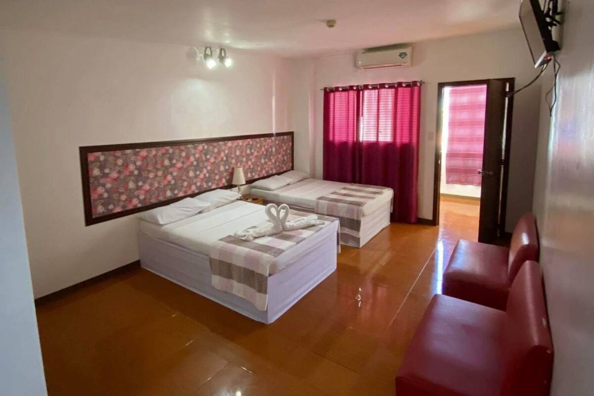 A hotel room with two beds, a red sofa, a large mirror, and a window with curtains.