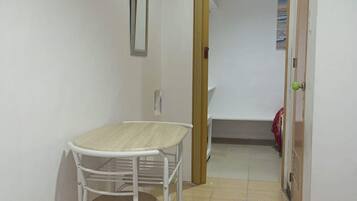 Una habitación pequeña y limpia con una mesa y una silla blancos, una puerta de madera y piso de baldosas.