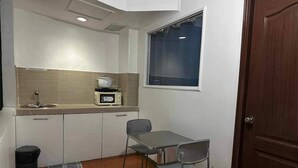 Cozinha compacta com micro-ondas, pia e pequena mesa com uma cadeira.