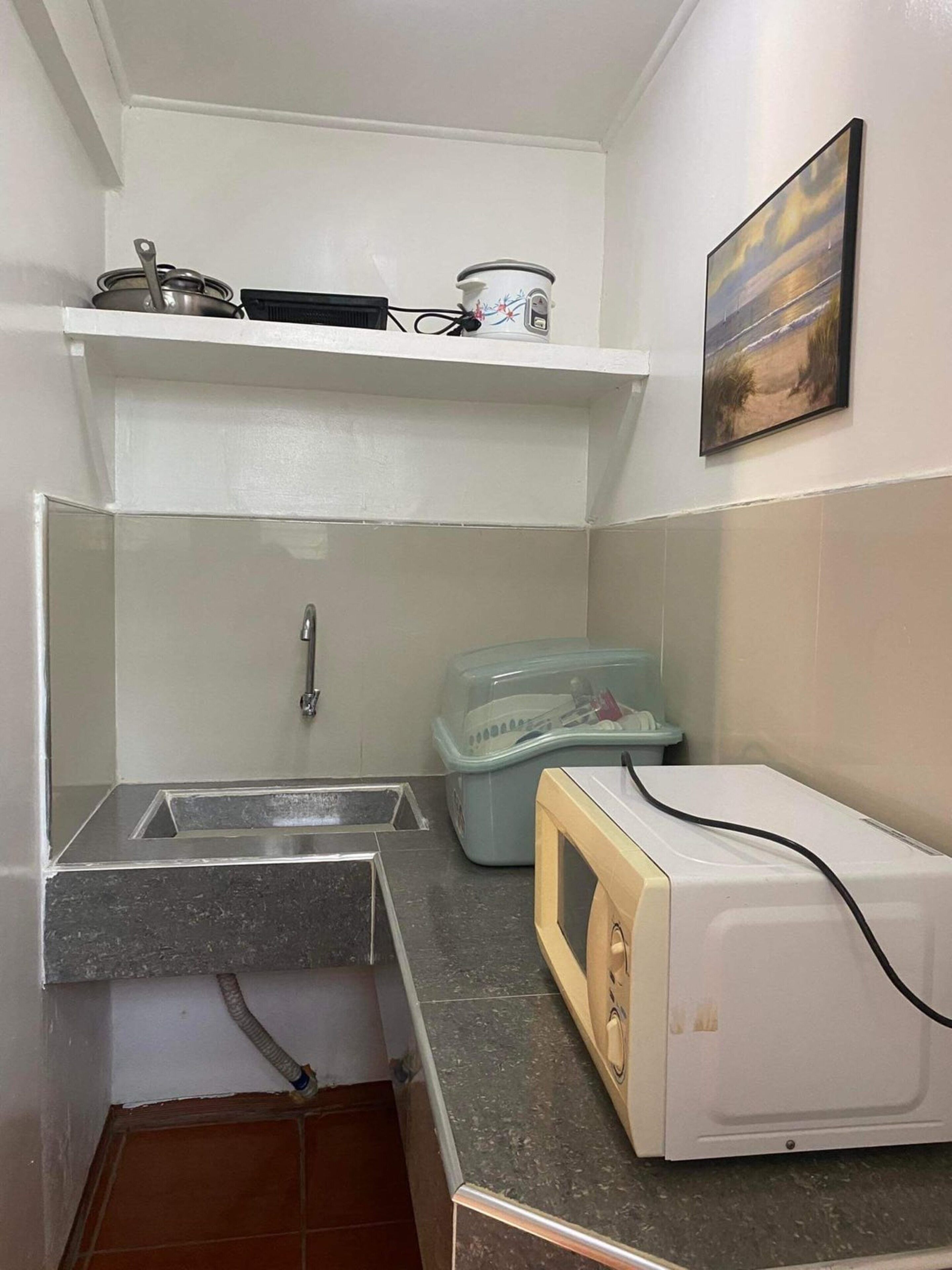 Una kitchenette pequeña con un microondas, un lavabo y un estante sobre la encimera.