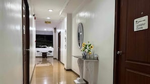 Corredor de hotel com balcão de recepção, área de refeições com mesa e cadeiras e sinal com orientações de saúde.