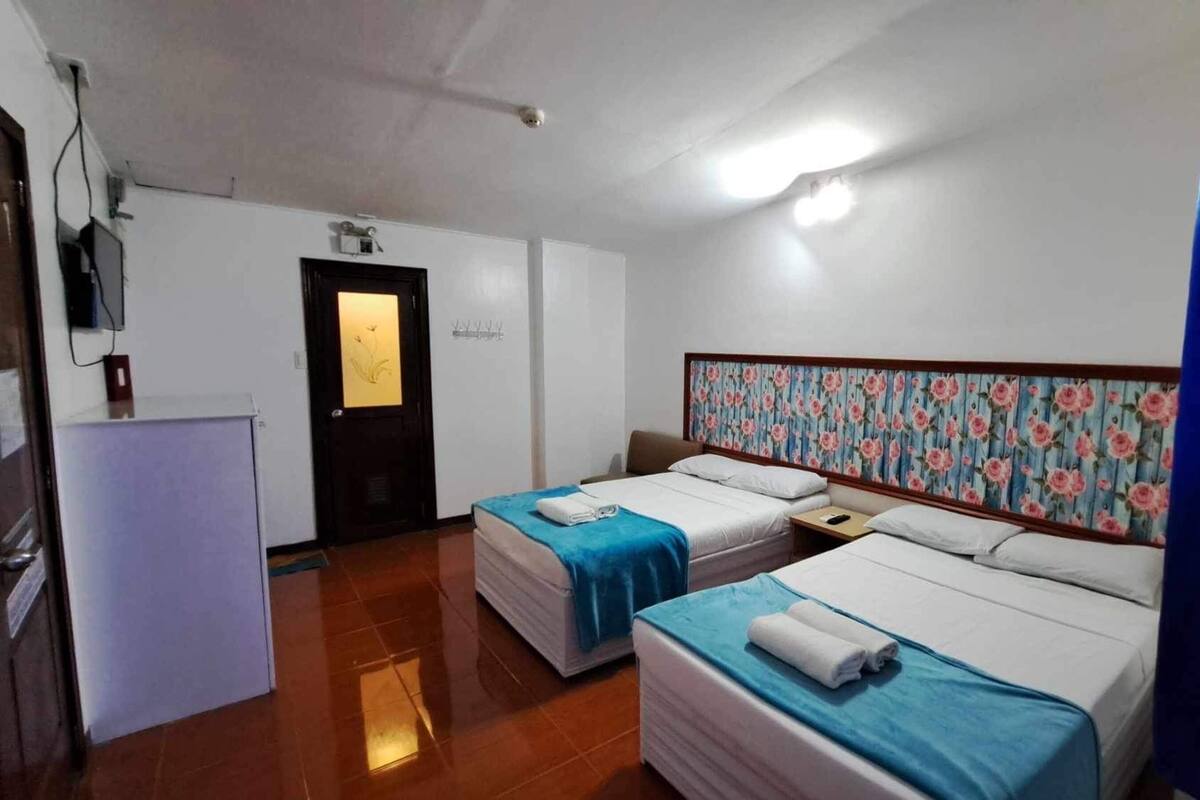 A hotel room with two beds, a desk, a refrigerator, and a door with a floral pattern.