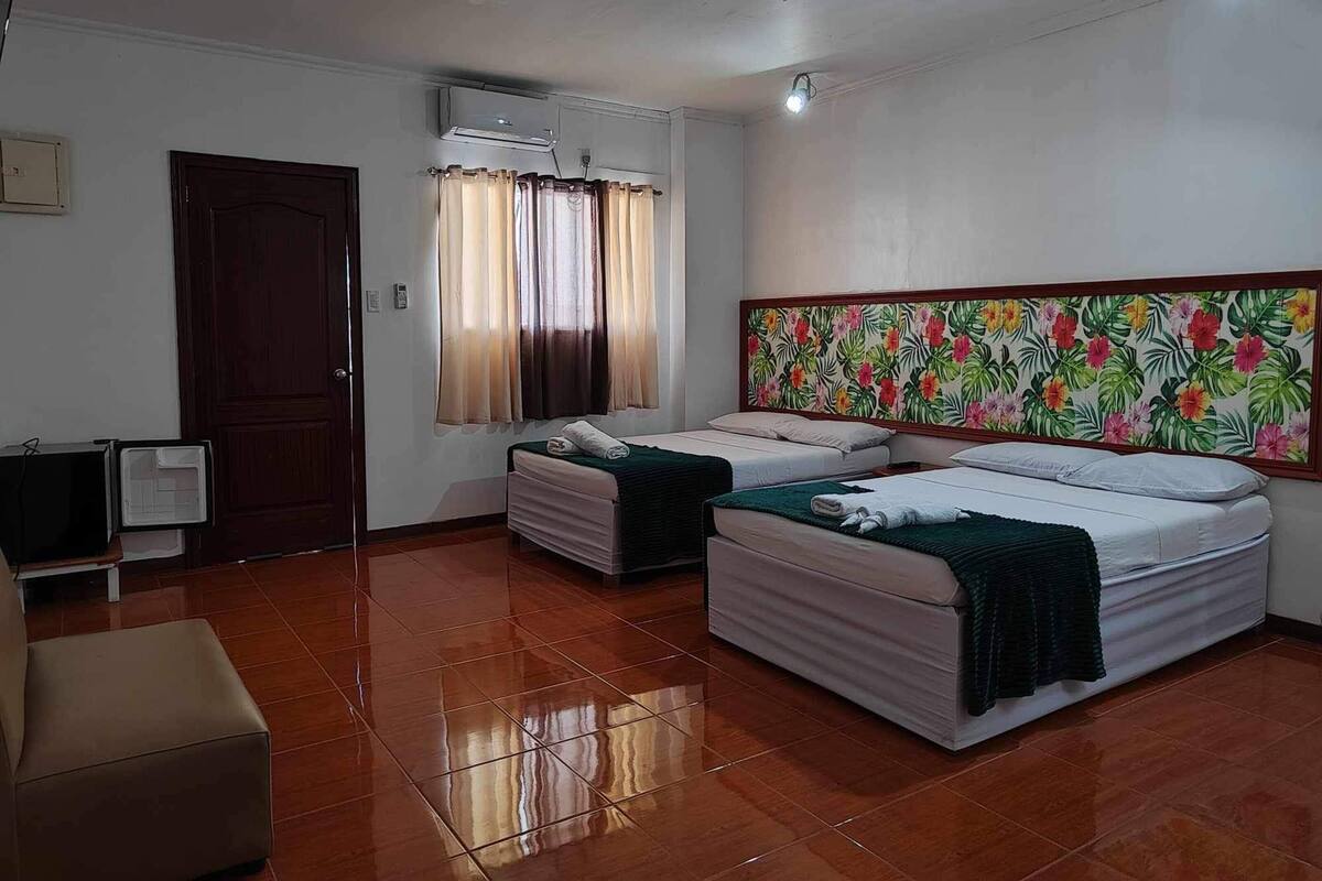 A hotel room with two beds, a TV, a desk, and a large floral mural on the wall.