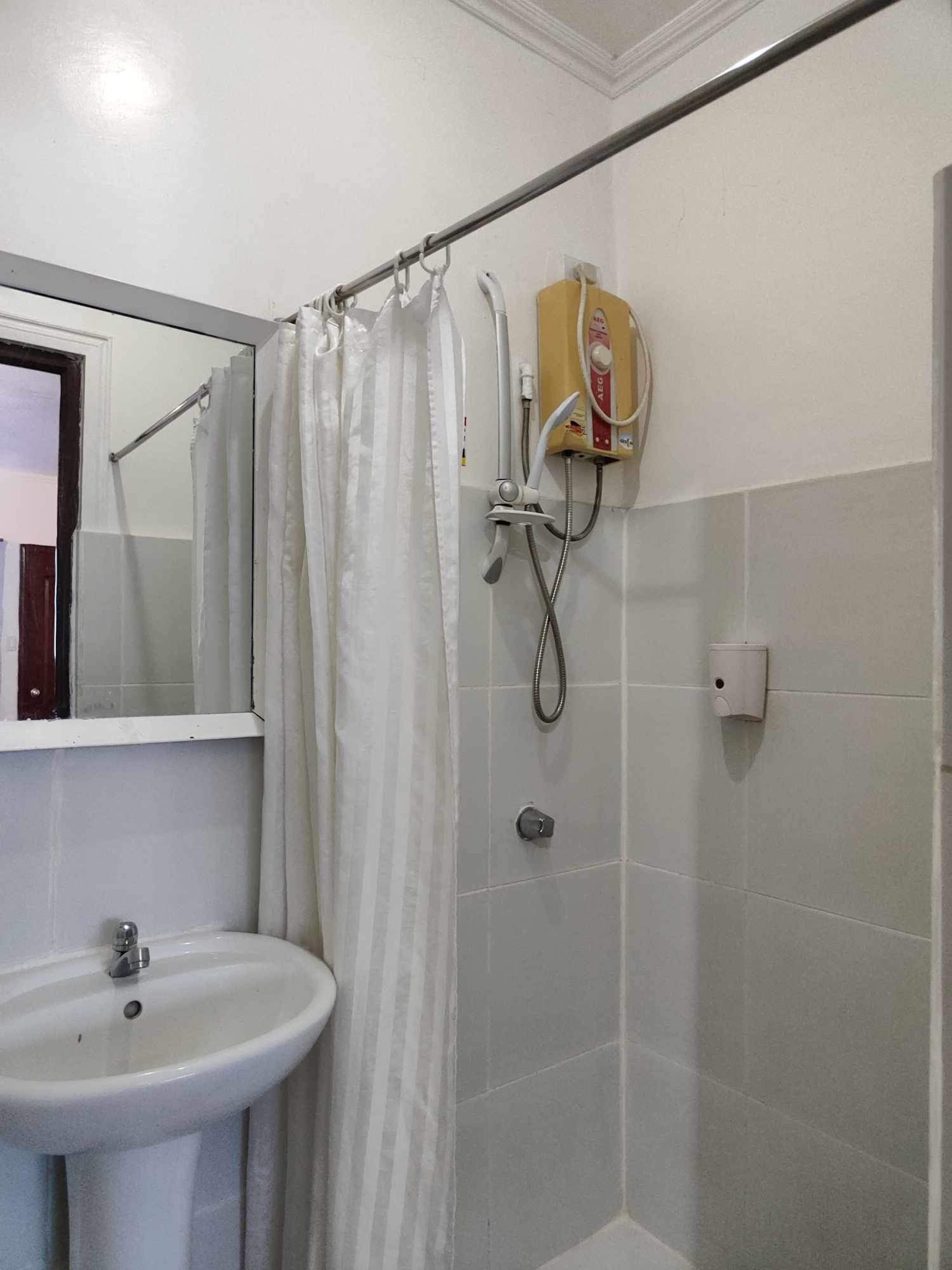 Une salle de bain avec un lavabo blanc, une douche avec un rideau et un porte-serviettes.