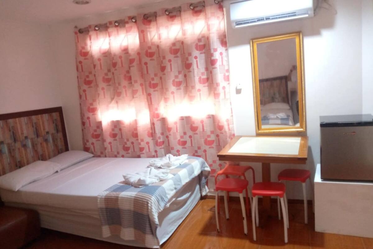 A bedroom with a bed, a desk, two chairs, and a mirror.
