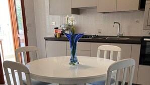 Une cuisine moderne avec des meubles blancs, une table de salle à manger ronde entourée de quatre chaises, et un vase bleu contenant des fleurs blanches.
