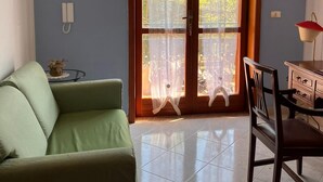 Une pièce avec un canapé vert, une chaise en bois, une table à manger et un lustre.