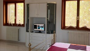 Une chambre à coucher comprenant un lit, une télévision, une armoire et deux fenêtres avec des rideaux.