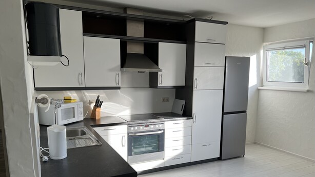 Una cocina moderna con armarios blancos, encimera negra, horno empotrado, microondas y refrigerador.