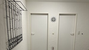 Un pasillo con dos puertas blancas, un perchero metálico y un felpudo negro.