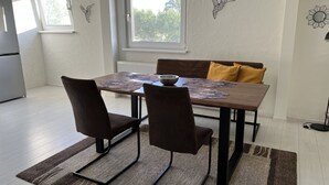 Un comedor con una mesa de madera, dos sillas, un cojín amarillo y una ventana con vistas a árboles.