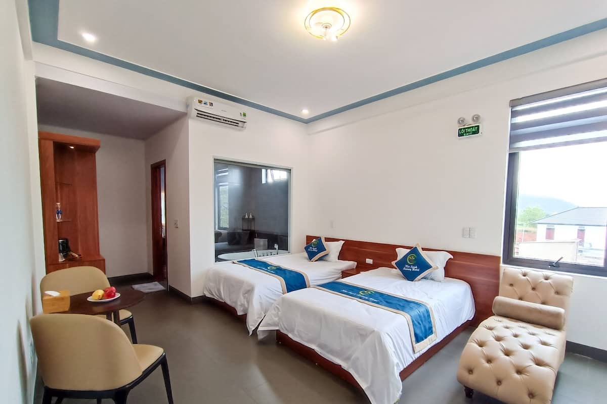 A hotel room with two beds, a chair, a desk, and a window.