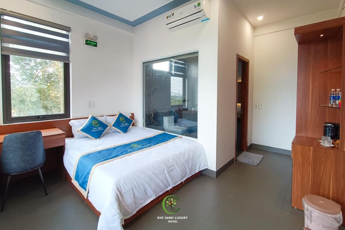 A hotel room with a bed, a desk, a chair, a wardrobe, and a shower area.