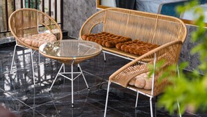 A wicker sofa and chairs with cushioned seats, a glass table, and a balcony with a marble floor.