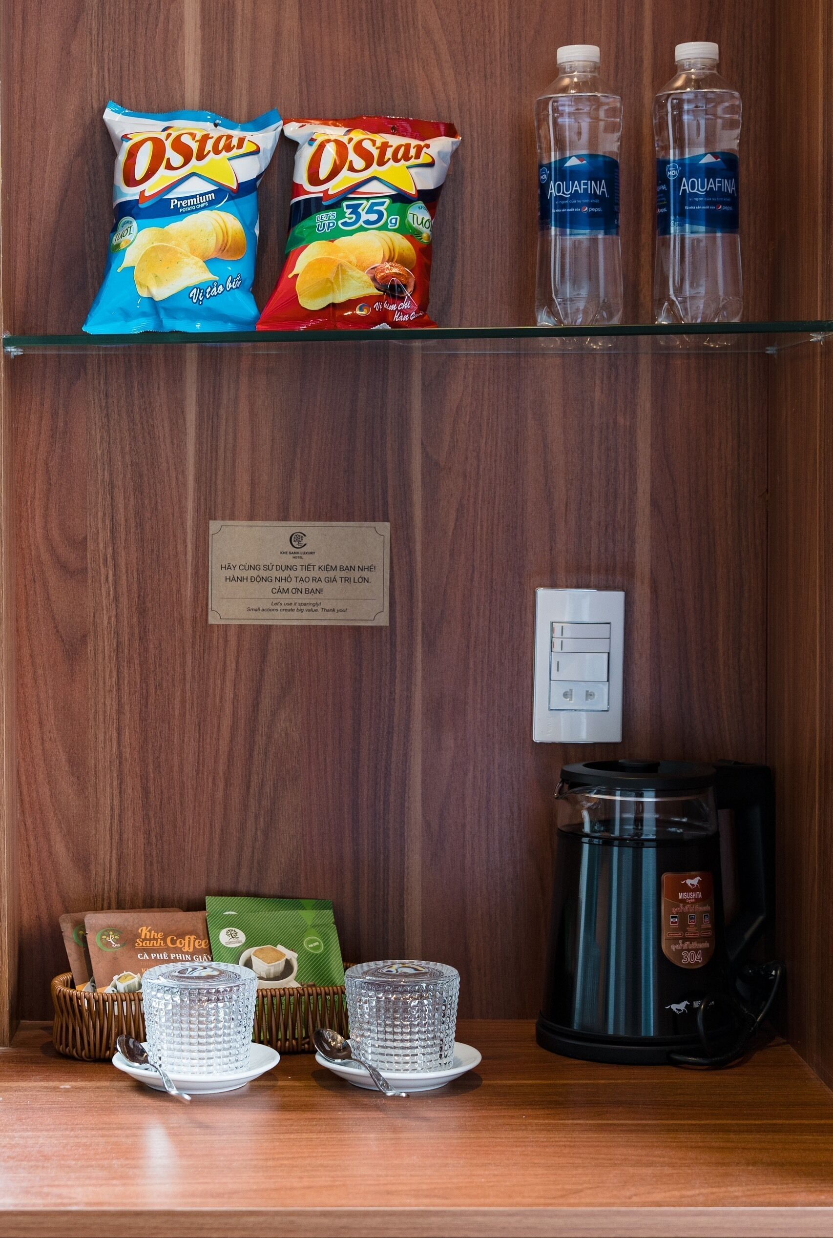 A hotel room with snacks, bottled water, and coffee-making equipment.