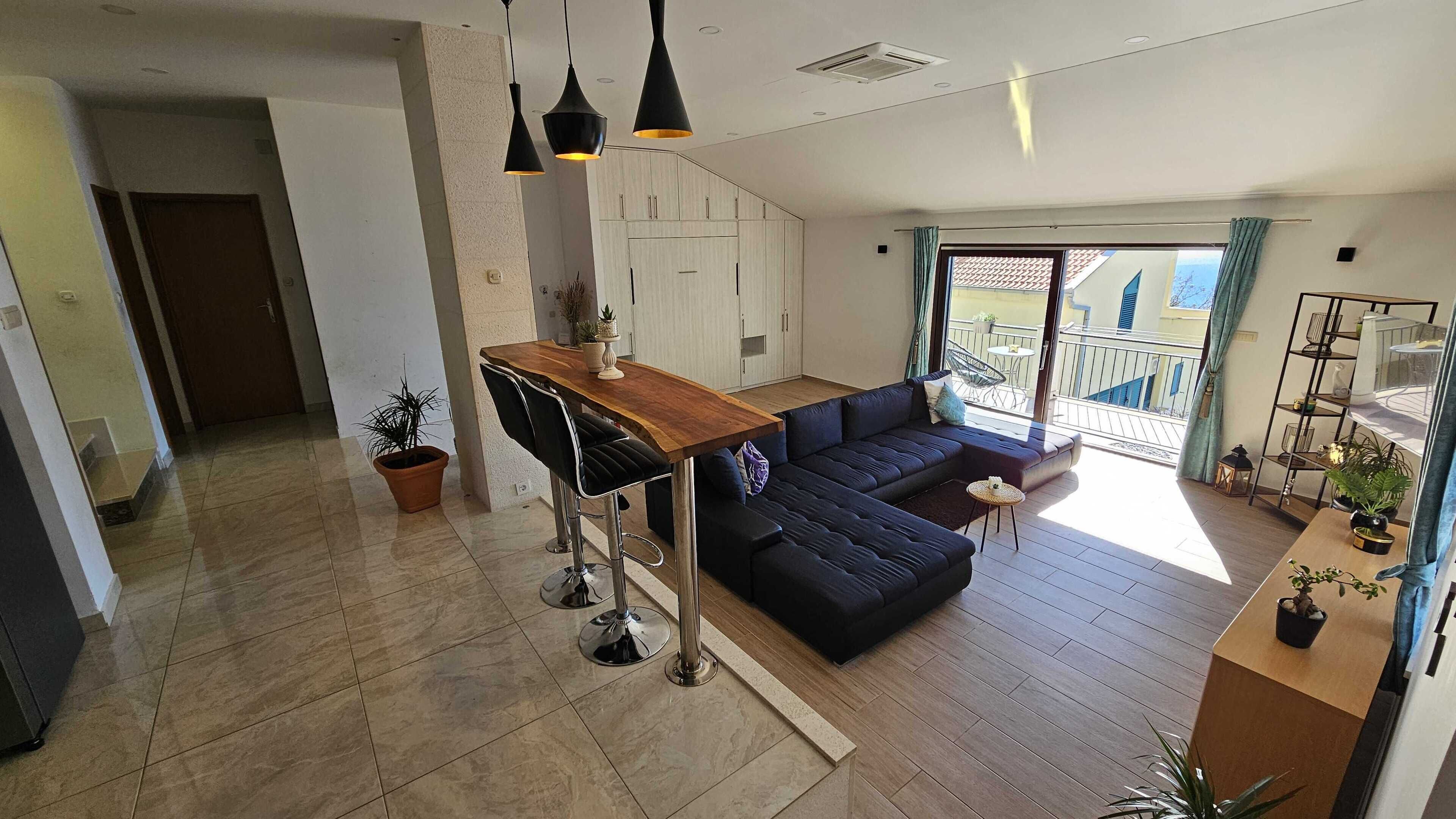 A modern living room with a dark blue sofa, a wooden coffee table, and a kitchen area with light-colored cabinets.