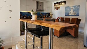 A modern kitchen with a wooden bar area, stainless steel bar stools, and pendant lighting. - Holiday Home Sunrise (Omis)