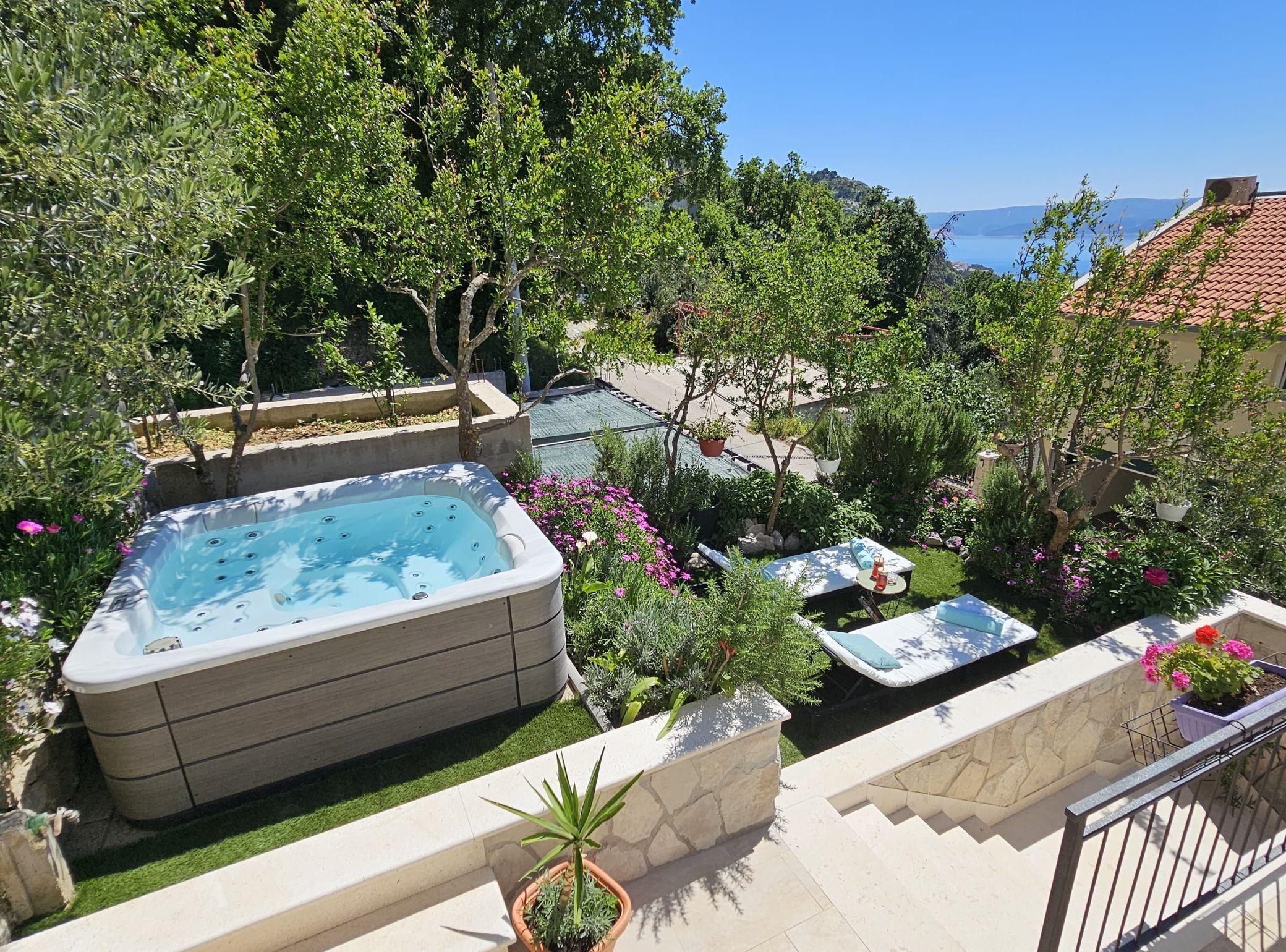 Un bain à remous entouré d’une végétation luxuriante et de plantes en pot, avec une vue sur la mer en arrière-plan.