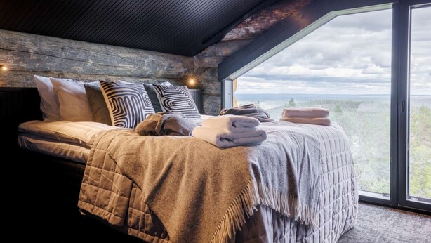 A bedroom with a large bed, wooden headboard, and a view of a forested landscape through a large window. - Luxury Villa Utsun Otso with breathtaking landscapes.  (Sirkka)