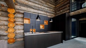 A modern kitchen with a central island, dark cabinetry, and a wooden log wall. - Luxury Villa Utsun Otso with breathtaking landscapes.  (Sirkka)