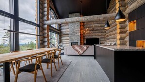 A modern log cabin interior with a stone fireplace, wooden dining table, and black pendant lighting. - Luxury Villa Utsun Otso with breathtaking landscapes.  (Sirkka)